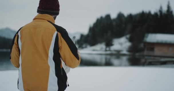 驚くほどの大きな湖と雪に覆われた森林を用いた木造住宅の素晴らしい風景の着いたカメラの前で彼の右の宛先を検索する地図で歩く観光客のビデオ キャプチャと — ストック動画