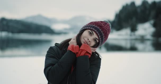 Closeup πορτρέτο του μια νεαρή κοπέλα δίπλα σε μια μεγάλη λίμνη και τα χιονισμένα βουνό κοιτάζουν κατευθείαν την κάμερα και να ποζάρει δείχνει μια μεγάλη καρδιά από χέρια είναι πολύ χαρούμενος τουρίστα που έφτασε στο καταπληκτικό τοπίο — Αρχείο Βίντεο