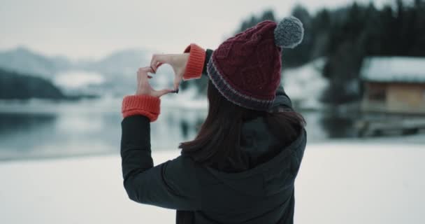 Genç Bayan turist bütün güzelliği hayran doğa ile bir büyük mavi göl ve karlı orman ve dağ, elinden büyük bir kalbi gösterilen çok mutlu olduğu. — Stok video