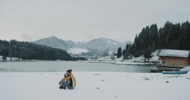 Wonderful place of nature big lake and mountain with snowy forest tourist have a little time of relaxing and admiration of all the beauty, drinking a cup of tea and sitting on the snow beside a — стоковое видео