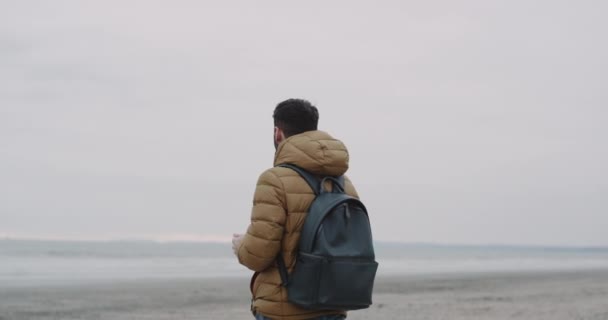 Porträt eines gutaussehenden Typen mit Handy am Strand des Meeres. Junge schaut auf Handy-App. 4k. — Stockvideo