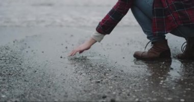 Adam ayakta yağmur gün sahil üzerinde o onun el ve atmak ıslak kum elinden ıslak kum indirdi