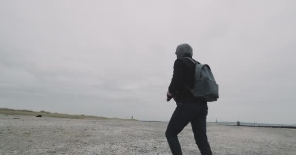 Lycklig man gå genom grå stranden efter ett regn på frysning dag bredvid en havsstrand. — Stockvideo