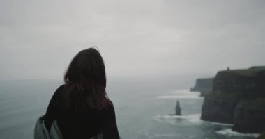 İyi görünümlü kız kayalıklarla top var bir meditasyon booth onu kendine, o stand ile kamera okyanusa geri.