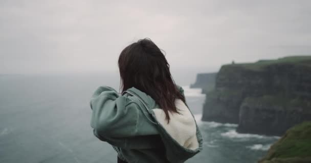 Belle jeune femme au sommet des falaises se déplaçant lentement devant la caméra, elle regarde droit devant la caméra et sourit un peu lentement. 4k — Video