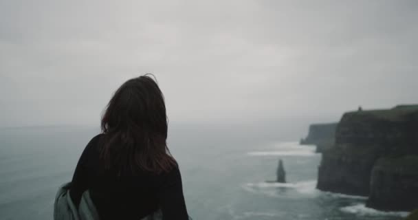 Hodně pěkná holka v horní části útesů a mají vysoké průměrné meditace její já, ona stojan zpět do fotoaparátu při pohledu na oceán. — Stock video