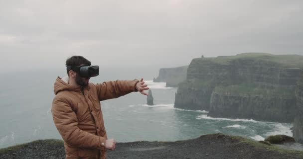 VR tid för en ung turist i toppen av klipporna, han utforskar den plats som använder en Vr och känsla imponerad, stå på toppen av Cliffs of Moher. 4k — Stockvideo