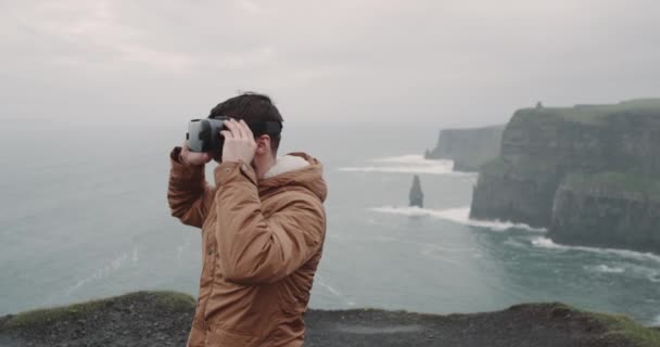 Gros plan homme utilisant des lunettes VR pour voyager à travers le monde, il se tient sur le sommet des falaises de Moher et exalté en utilisant VR . — Video