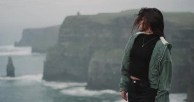 Kameranın üst kısmında, etkilendim Moher kayalıklarla önünde sevimli küçük esmer Bayan yavaş hareket kamera önünde yerleştirin ve ile okyanus görünümüne çevirir.