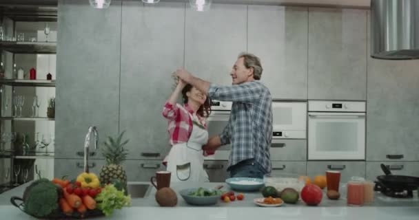 Dacing couple d'âge mûr tout en préparant le petit déjeuner sain dans la cuisine avec un design moderne incroyable. 4k — Video