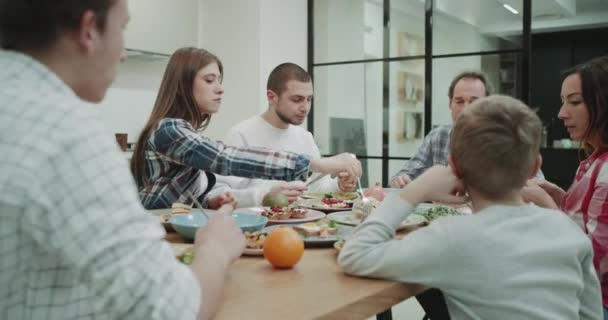 Зрілі батьки та їхні діти проводять домашню вечерю разом, вони дуже голодні, їдять їжу та відчувають задоволення, що вони разом у сучасному дизайні кухні повільні рухи — стокове відео