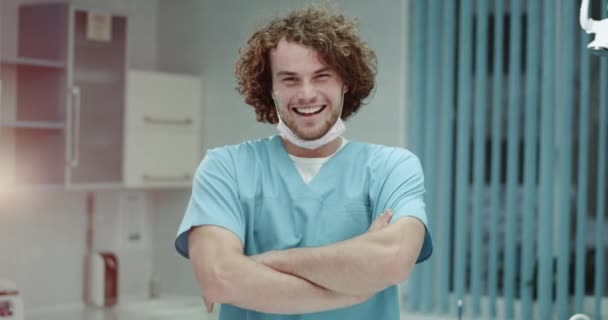 Retrato de un joven cirujano sonriente o un médico que se pone una máscara quirúrgica y mira directamente al fondo de la cámara moderna sala de la clínica. tiro en épica roja — Vídeo de stock