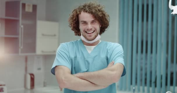 Retrato de un joven cirujano sonriente o un médico que se pone una máscara quirúrgica y mira directamente al fondo de la cámara moderna sala de la clínica. tiro en épica roja — Vídeos de Stock