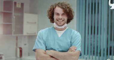 Kıvırcık saçlı ve mükemmel diş kliniği, Genç adam elinde bir modern klinik oda ile gesticulating ziyaret için davet gülümseyen mutlu Doktor portresi.