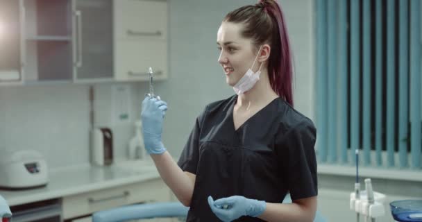 Mulher dentista jovem em uma sala de clínica moderna olhando diretamente para a câmera e segurando uma seringa com medicação pronta para uma injeção. 4k — Vídeo de Stock