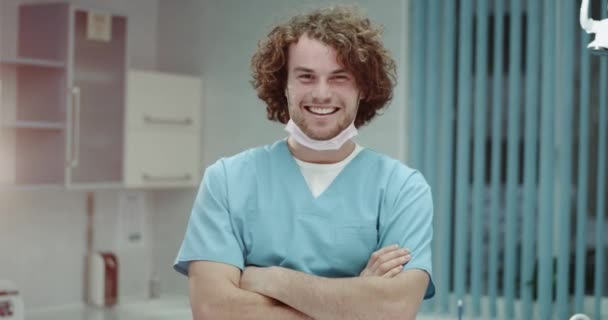 Porträtt av leende glada läkare med lockigt hår och perfekta tänder bjuder in dig till att besöka hans klinik, ung man gestikulerade med händerna, i en modern klinik rum. — Stockvideo