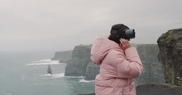 Charismatic young woman using a VR on the top of the Cliffs she is very impressed and smiling large , closeup to the camera she standing beside the shore of the Cliffs. 4k. shot on red epic — Stock Video