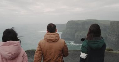 Okyanus ve kayalıklarla güzel manzaralı muhteşem manzara yeri üç arkadaş geldi, onlar kayalar shore duran üst ve görünümü hayranım. 4k