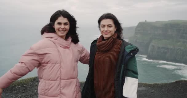 幸せな 2 人の女性は互いを抱いて彼らに笑みを浮かべてカメラを直視モハーの断崖の屋上に驚くべき場所に到着しました。4 k. 遅い動き — ストック動画