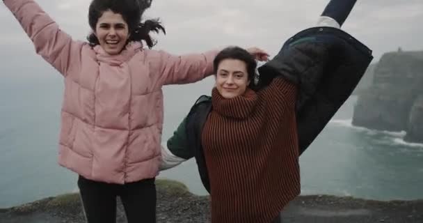 Springen en gevoel onder de indruk twee dames aangekomen op de mooiste plek op de wereld Cliffs of Moher, ze zijn erg blij staande op het dak naast de oever van de kliffen, prachtige oceaan — Stockvideo