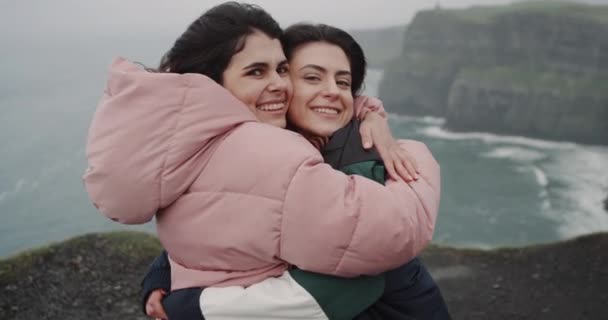 Vrij twee dames op zoek voor de camera op het dak van verbazingwekkende kliffen houden elkaar en tonen een grote zoals naar de camera. — Stockvideo