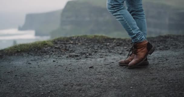 Detalles primer plano turista caminando a la orilla de los acantilados con botas marrones, se detuvo al lado de la orilla, increíble paisaje de océano y acantilados alrededor . — Vídeo de stock