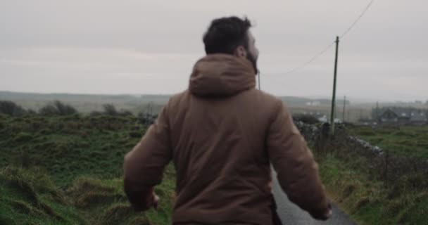 Feliz turista caminhando pela estrada no meio do campo, ele pulando, na hora da noite. movimentos lentos — Vídeo de Stock