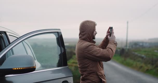 Parada turística con el coche en medio de la carretera en el campo y tomar algunas fotos de la puesta del sol, paisaje increíble alrededor, utilizando un teléfono inteligente para fotos . — Vídeos de Stock