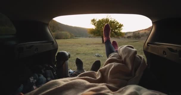 Paar hebben een reis met de auto, ze hebben een stop, vaststelling van op de kofferbak auto, met een gezellige sokken en een grote Thermoskan van warme dranken te wachten voor zonsondergang spelen grappig met benen. 4k — Stockvideo