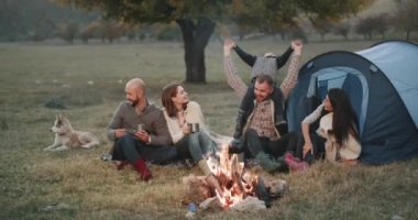 Doğa iki aile piknik vakit akşam kamp ateşi altındadır ve çadır, küçük oğlu ile oynama baba yanında tüm oturma etrafında mutlu, küçük husky köpek.