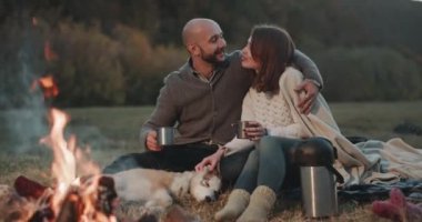 Birlikte birbirlerine sarılma ve öpüşme romantik harcama zaman akşam kamp ateşi zamanında güzel bir husky köpek ile karizmatik genç bir çift için. 4k