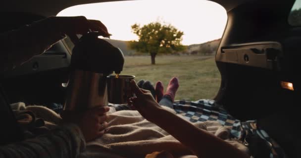 Pareja romántica pasar un buen rato juntos en el picnic que yacen en el maletero del coche y con un calcetines acogedores usando un termo beber un poco de té caliente. 4k . — Vídeos de Stock