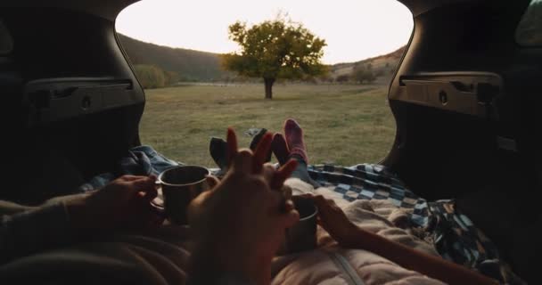 車のトランクのカップルで手と日没を待っているフロント ティーを保持している彼らの居心地の良いソックス楽しい時間一緒に着て、毛布があります。4 k — ストック動画