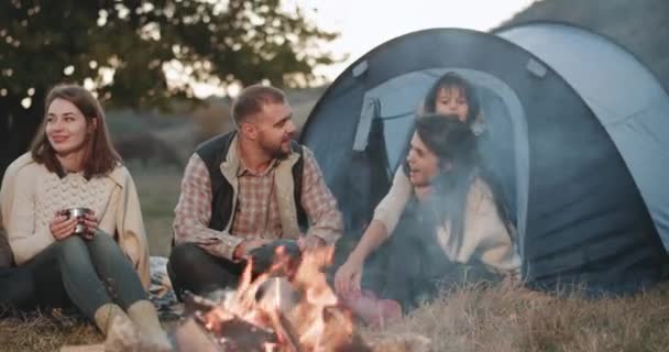 Küçük bir çocuk ve onların arkadaşları ile güzel genç aile piknik doğa, onlar kamp ateşi yanında zaman geçirmekten mutlu ortasında bir çadır ile. — Stok video