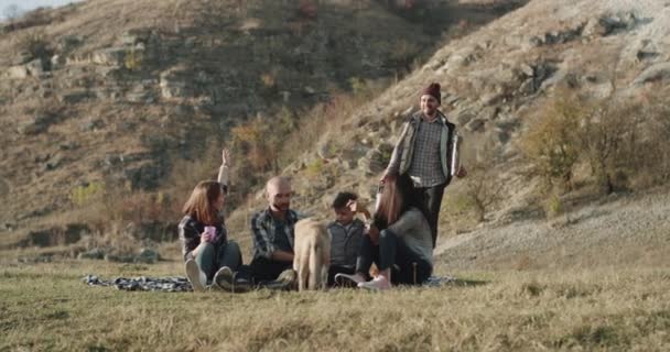 Zwei Familien picknicken mitten in der Natur, am Abend setzen sie sich auf das Gras, spielen mit einem niedlichen Husky-Hund und bereiten sich auf einen heißen Tee vor.. — Stockvideo