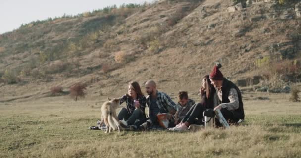 Идеальное время для друзей на пикнике лежа на траве проводить теплое время вместе пить чай и играть с их хаски собака, милый маленький мальчик есть некоторые закуски — стоковое видео