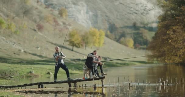 Drôle de temps à la nature, un garçon mignon avec son père et un ami de la famille passer du bon temps ensemble attraper des poissons du lac un petit chien husky mignon se promener. 4k — Video