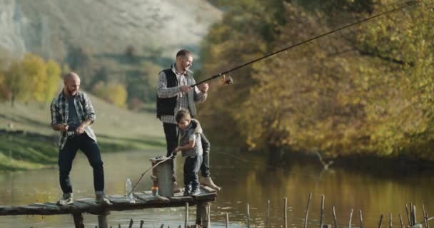 Zwei Männer und ein kleiner Junge fangen mit zwei Angelruten Fische aus dem See. — Stockvideo
