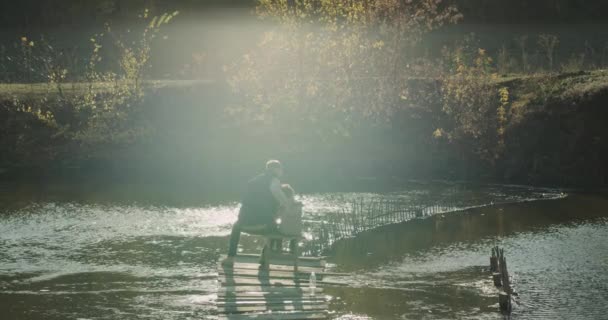 Maravillosa vista de un lago, papá y su hijo sentado en una silla en la parte superior del puente y la captura de peces desde el lago. movimientos lentos. 4h — Vídeo de stock