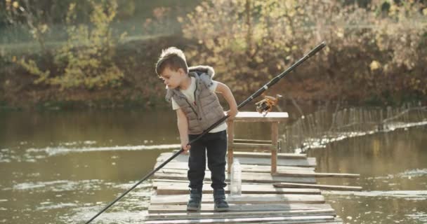 Piccolo ragazzo divertente insegnamento come pescare sul lago che tiene una grande canna da pesca . — Video Stock