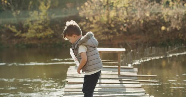 Roztomilý malý chlapec hraje s lahví u jezera, stojící na vrcholu mostu. 4k — Stock video