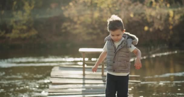 非常に素晴らしい小さな男の子湖の横にある橋の上に立って、大きなようなを表示するカメラを直視します。赤の叙事詩をショットします。 — ストック動画