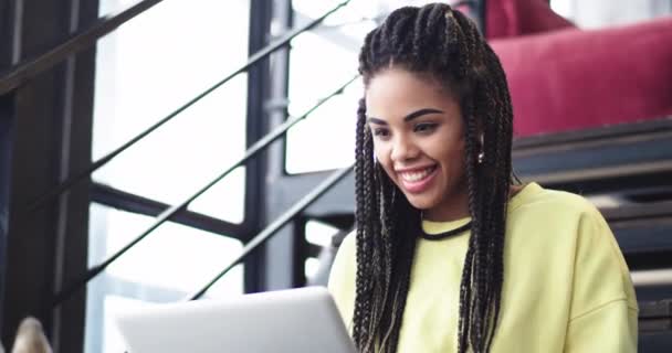 Primo piano molto bella giovane donna africana che lavora sul computer portatile, sul business center, lei seduta sulle scale, e un cane husky carino sono accanto a lei e carino giocano insieme. girato su epica rossa — Video Stock