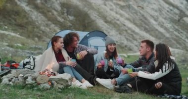 Gençler karizmatik grup bir piknik zaman kamp ateşi oturma ve bazı şarap veya çay içme dağ ortasında ve büyük bir konuşma var..