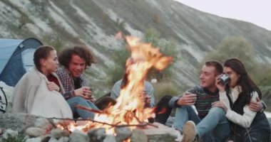 Üç bayanlar ve metalik bardak gülümseyen ve konuşma iyi bir ruh hali ile ve kamp ateşi, kamp bazı sıcak içecekler içme, iki adam.