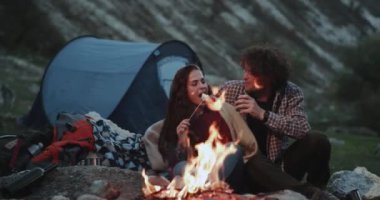 Romantik zaman kamp ateşi ve biraz şekerleme yemek ve ea sarılma bazı sıcak içecekler içme, yanında oturan dağda kamp birlikte bir çift için