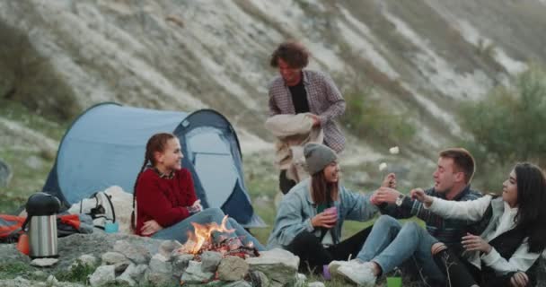 野营时间的朋友们在晚上的篝火旁寒意 吃棉花糖 男友为坐在篝火上的女友摘毯子 — 图库视频影像