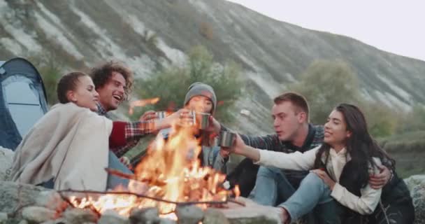 Gruppe von Freunden am Lagerfeuer sitzen und Tee oder ein paar heiße Getränke trinken, aus metallischen Tassen, sie sind sehr charismatisch. — Stockvideo