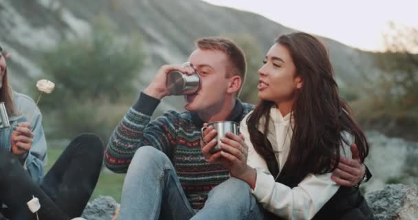 Amazing group of young teens at camping closeup eating marshmallows and drinking some hot drinks at bonfire. — Stock Video