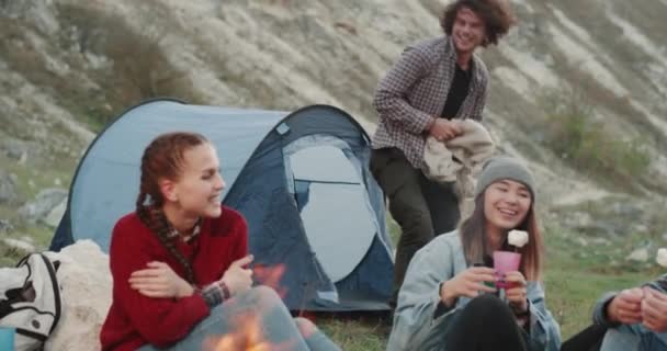 Abends auf dem Campingplatz reizendes Paar, Freund nimmt eine Decke und pflückt für seine Freundin, umarmt sie sehr nett, sie sitzen am Lagerfeuer. — Stockvideo